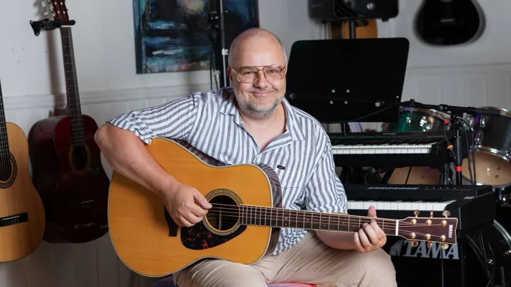 Bilde av Tommy som spiller gitar på musikkrommet med instrumenter i bakgrunnen