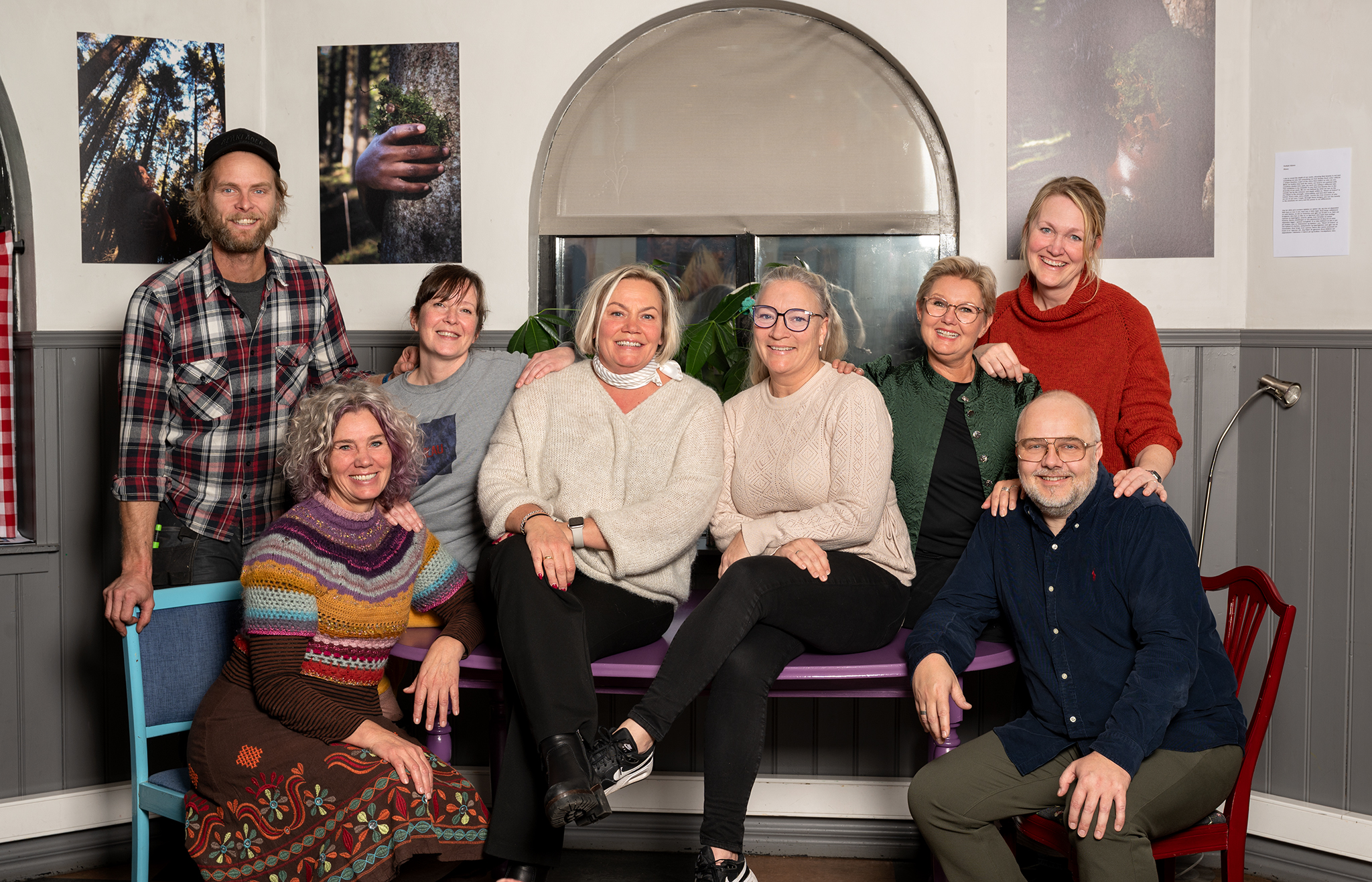 Gruppebilde av de 8 ansatte på Verket Larvik som sitter på og rundt et bord i kafeen. Alle smiler.