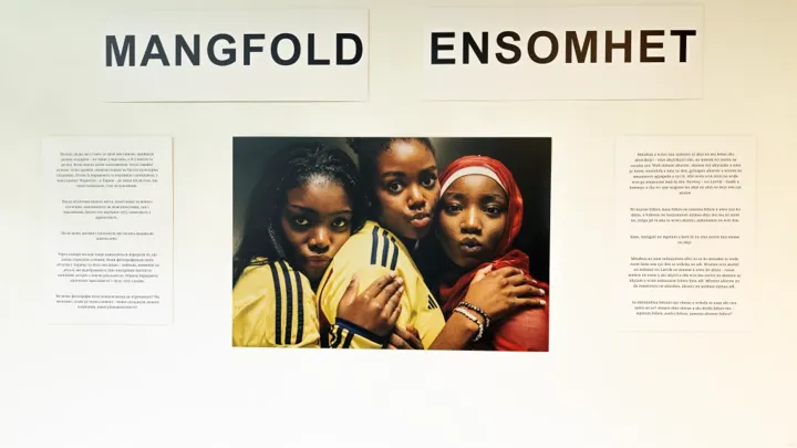 Tittel på utstilling sammen med hovedbildet av tre jenter som klemmer