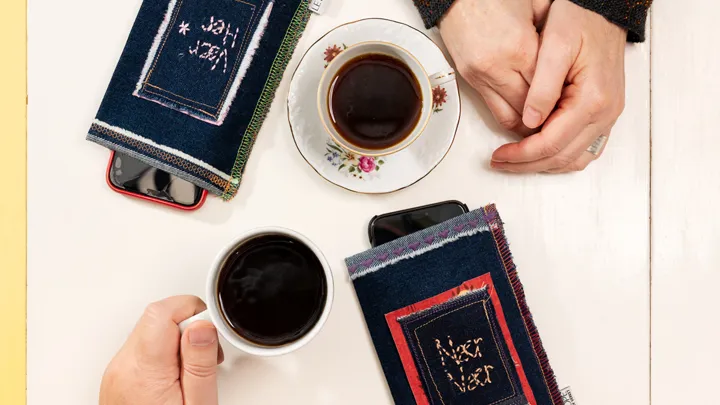 Nærbilde av to par hender på et bord med hver sin kaffekopp og hvilepose til mobil
