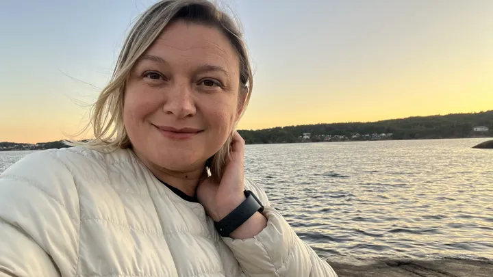 Portrett av blond kvinne stående foran havet.
