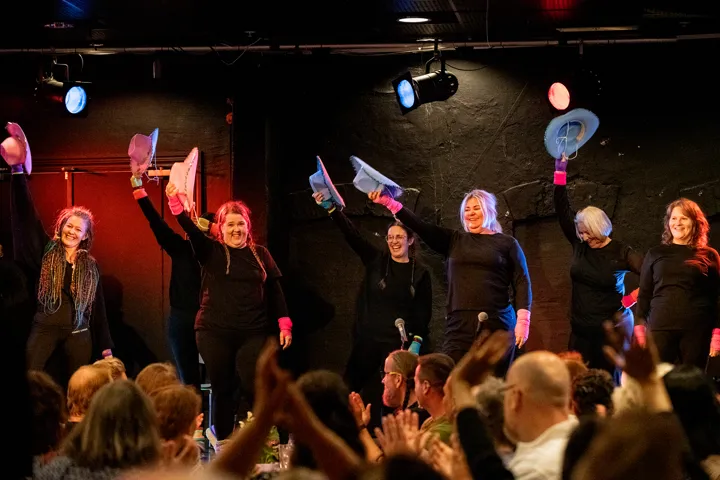 Dansegruppe på scenen i sorte klær og med fargede cowboyhatter, publikum i salen klapper,