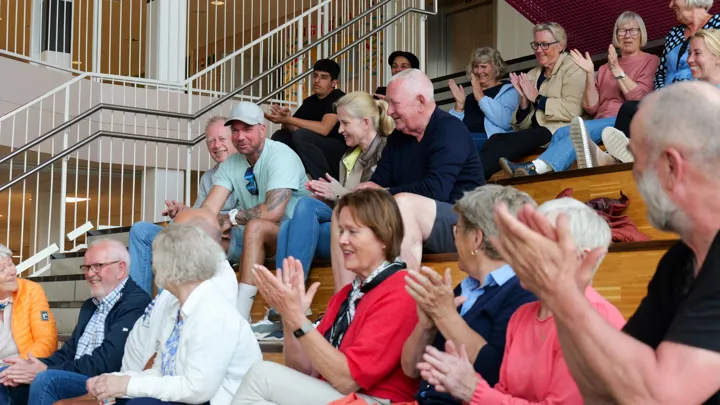 En forsamling sitter i en aula og klapper.