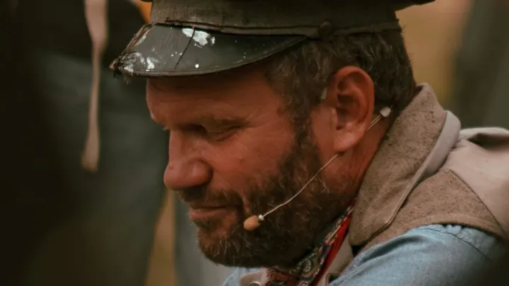 En mann med mikrofon sitter og ser skrått ned foran kameraet.
