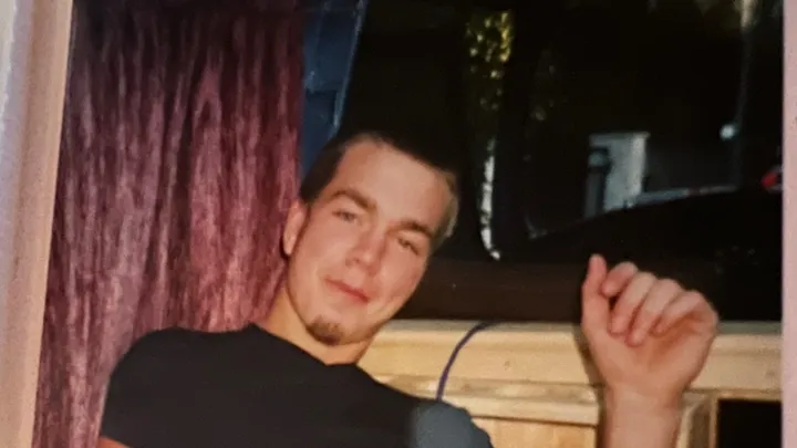 En ung mann sitter i en stol og smiler lurt til kameraet.